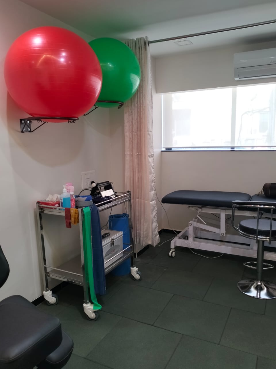 A calming therapy room at Dr. Chetna Clinic with a therapy table, a couch, and two chairs arranged around a glass coffee table. Artwork hangs on the wall, and exercise equipment is visible, suggesting a holistic approach to therapy.