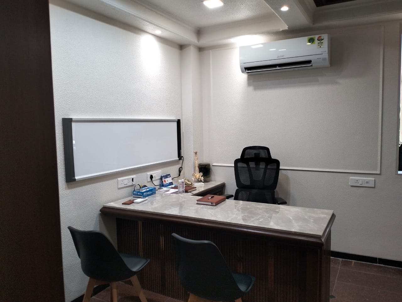 A spacious and well-lit consultancy room with a comfortable examination table, a couch for accompanying guests, and a coffee table. Medical equipment is subtly placed on the wall.