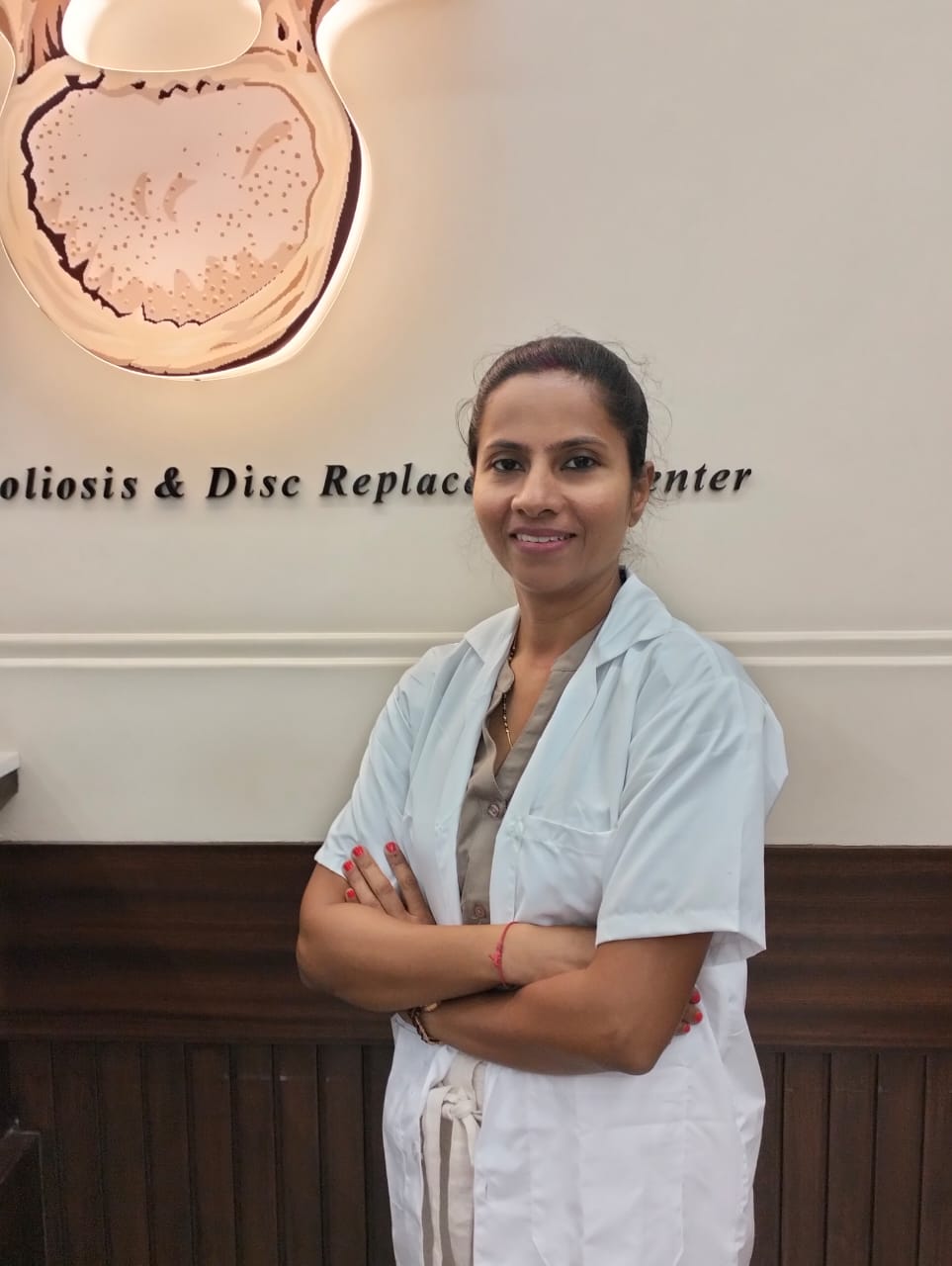 Dr. Chetna, wearing a white doctor's coat, stands confidently with her arms crossed in front of the entrance to the Kulkarni Spine Rehab & Physiotherapy Center