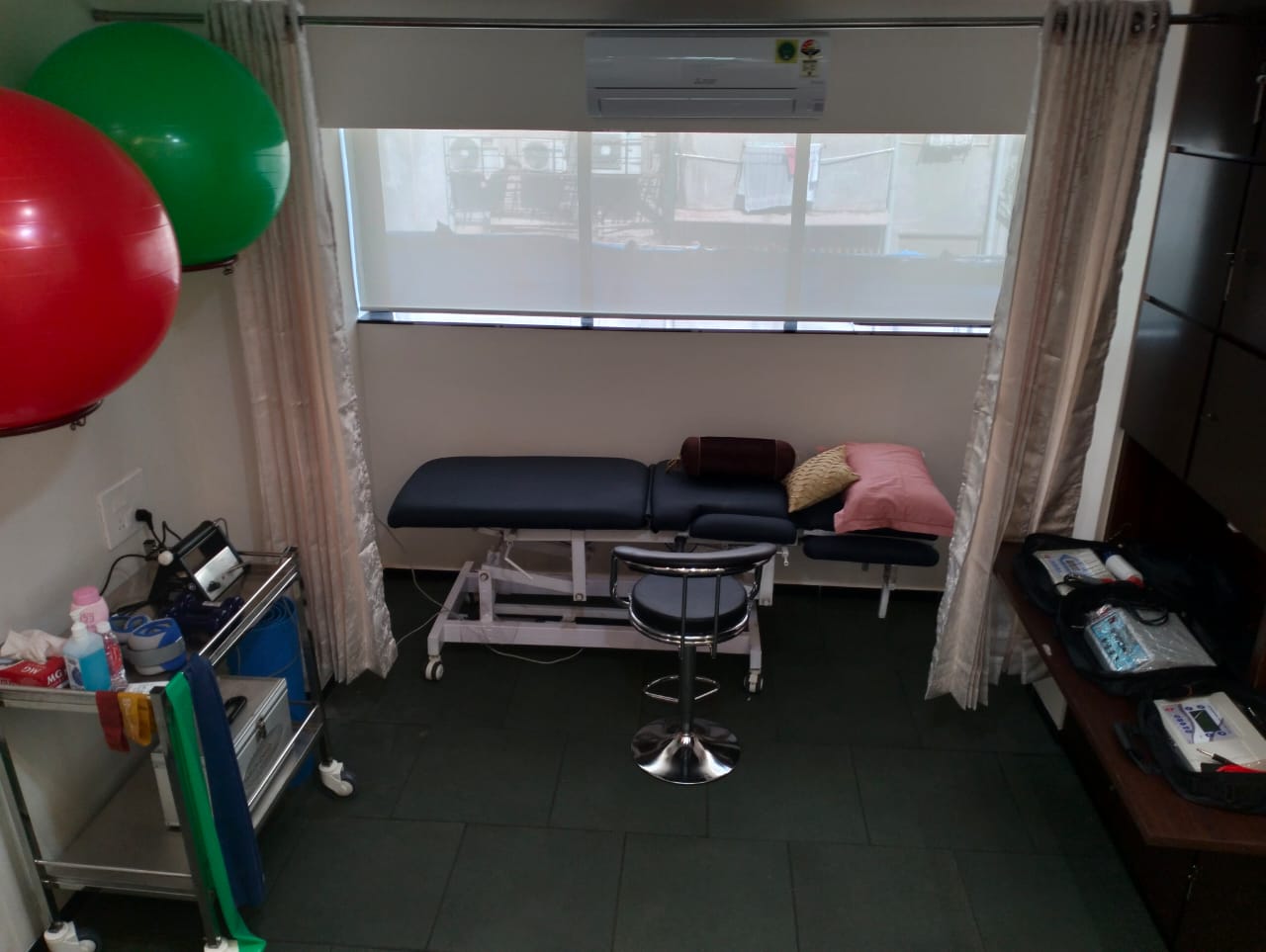 A calming therapy room at Dr. Chetna Clinic with a therapy table, a couch, and two chairs arranged around a glass coffee table. Artwork hangs on the wall, and exercise equipment is visible, suggesting a holistic approach to therapy.