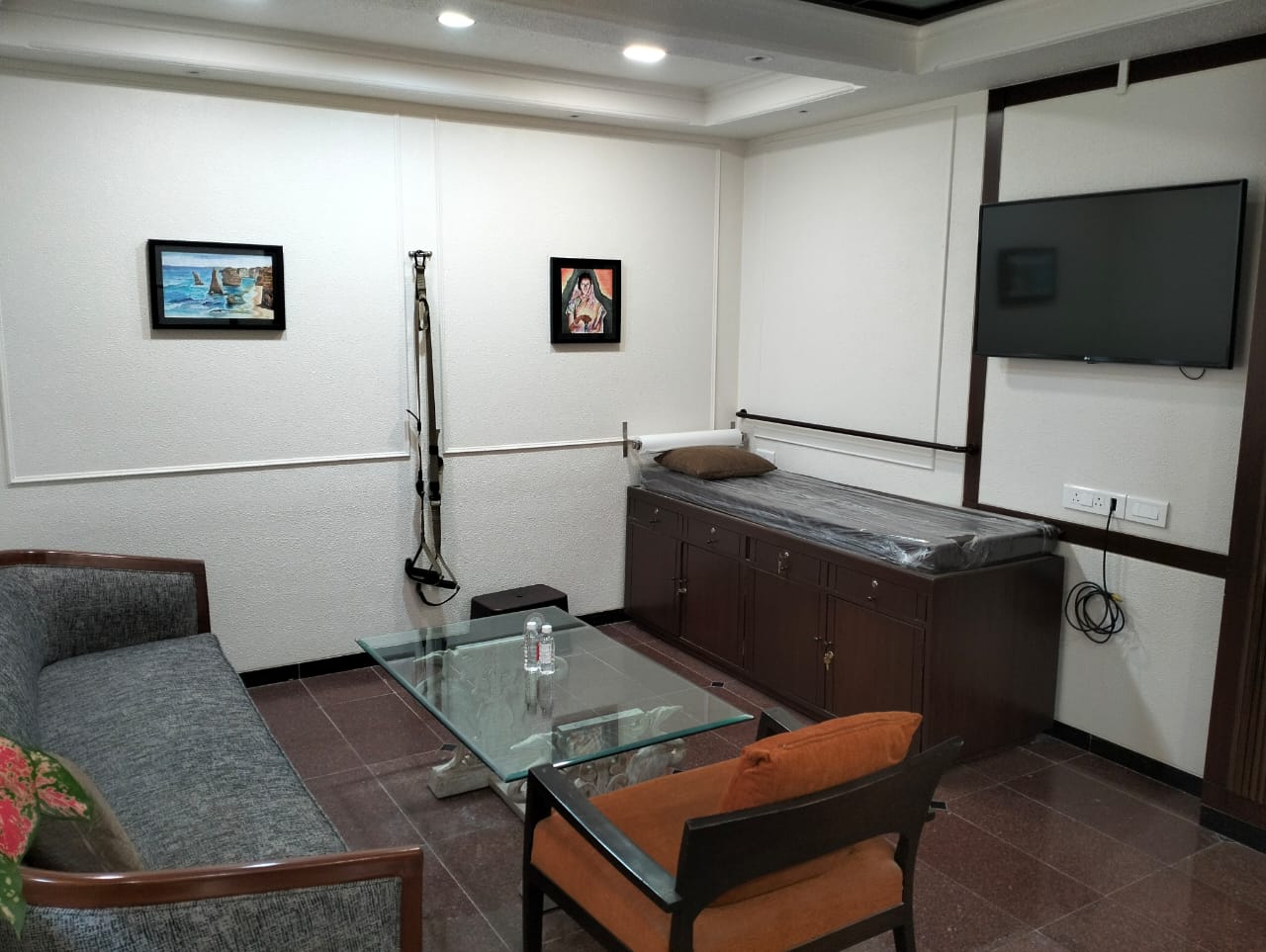 A calming therapy room at Dr. Chetna Clinic with a therapy table, a couch, and two chairs arranged around a glass coffee table. Artwork hangs on the wall, and exercise equipment is visible, suggesting a holistic approach to therapy.